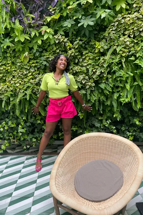 Tayler, smiling, standing in front of a lush green wall.